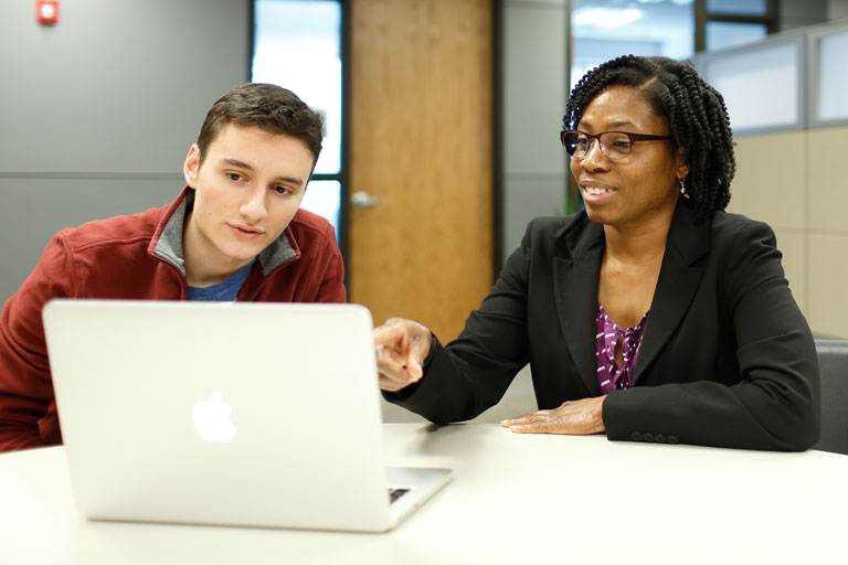 Male mentee and female mentor looking at laptop on table while mentor speaks.