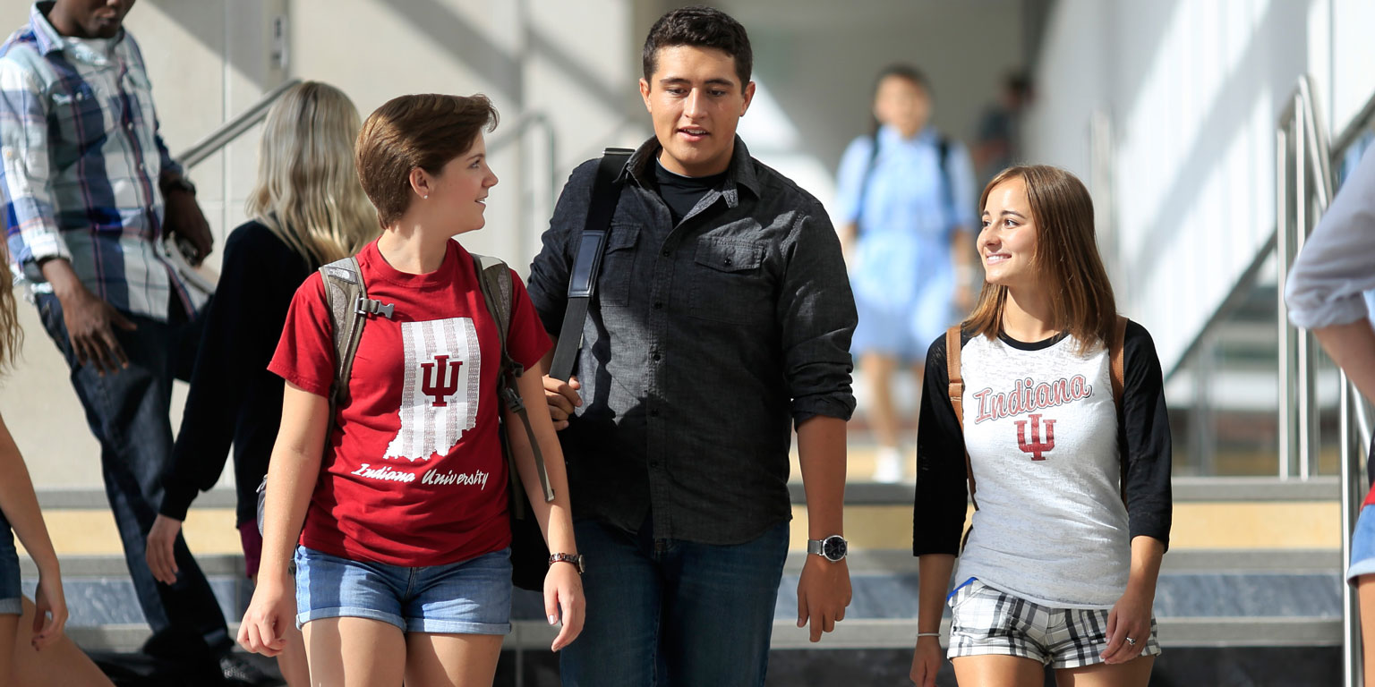 Three students walking hall steps speak with each other.